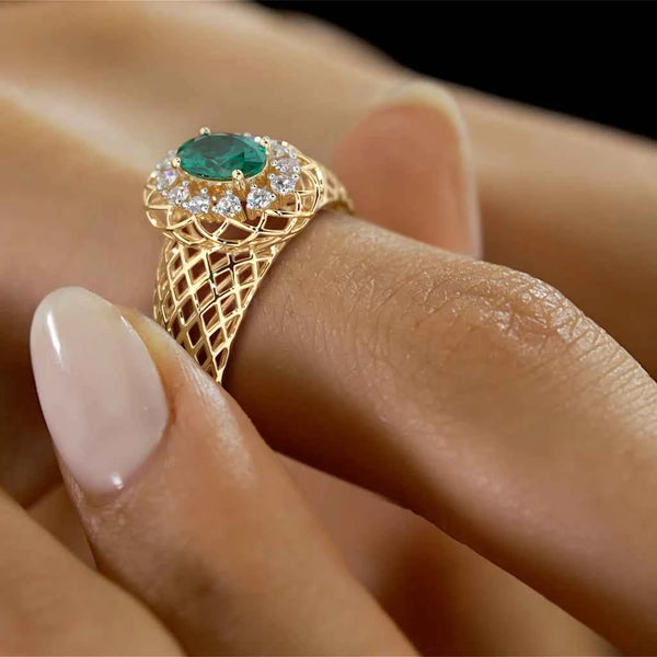 Gold openwork ring with oval green gemstone and diamond surround on finger