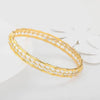 Gold bangle bracelet with openwork lattice and small clear stone accents