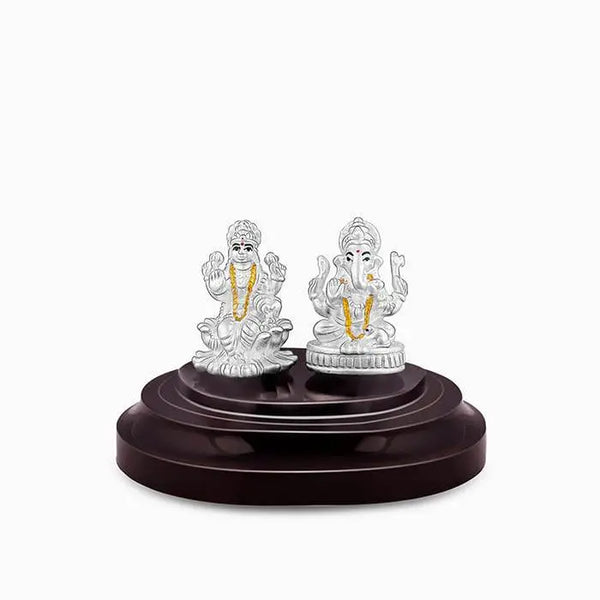 Silver Lakshmi and Ganesha idol under clear glass dome on dark base.