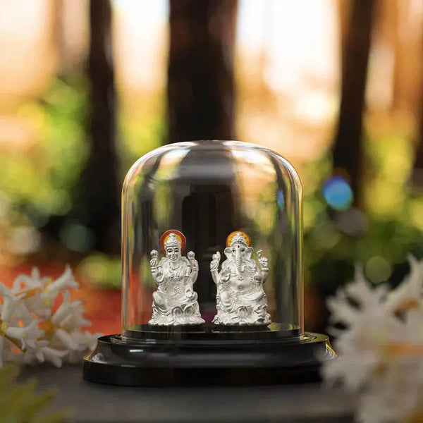Silver Lakshmi and Ganesha figurines under glass dome on dark base.